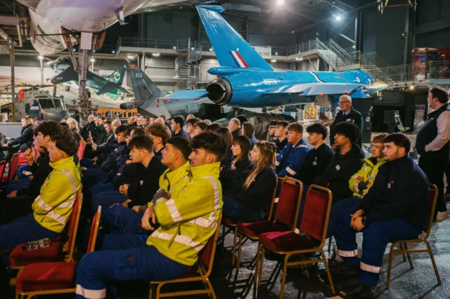A group of people sitting in chairs in front of an airplane.