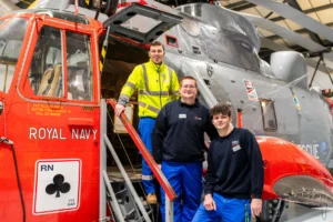 Three people standing in front of a Royal Navy helicopter