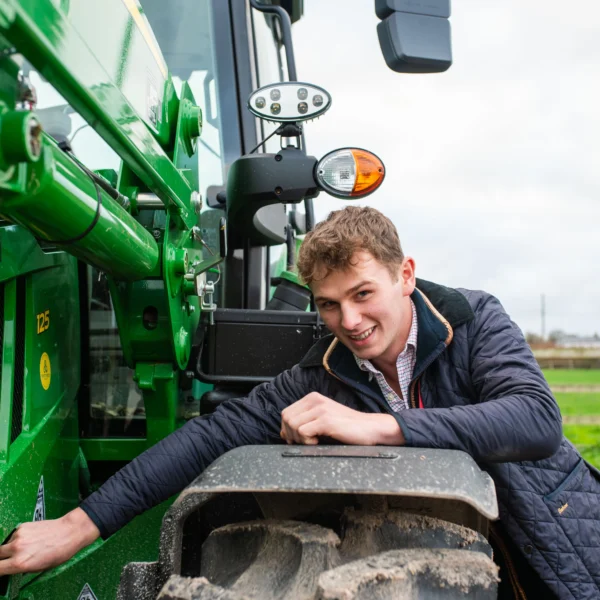 A young man leaning on a green tractor in a field.