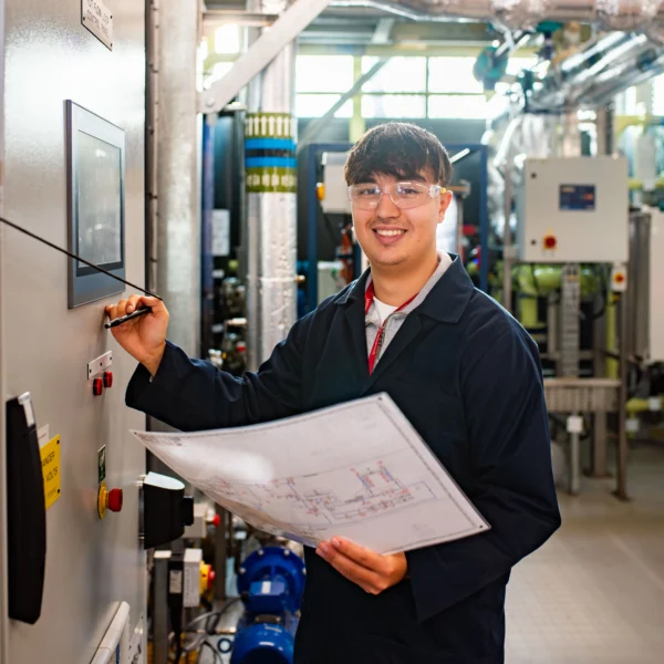 Male engineer in a lab coat reviewing a document and operating a control panel.