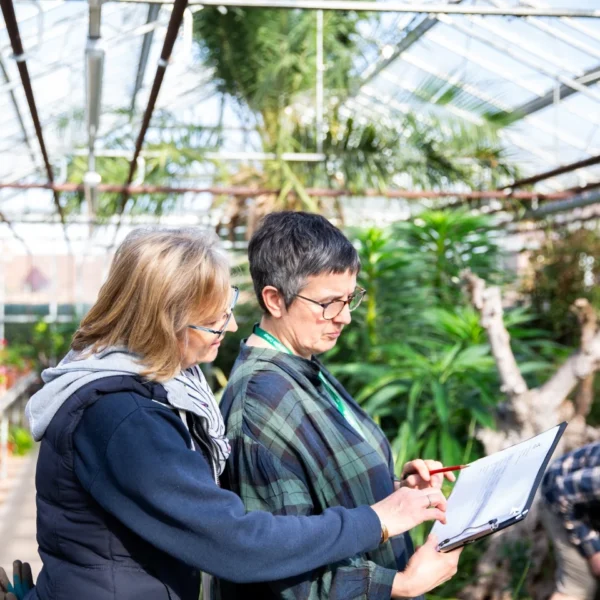 Two people looking at a piece of paper in a greenhouse.