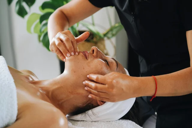 A skilled masseuse providing a facial massage to a serene client.