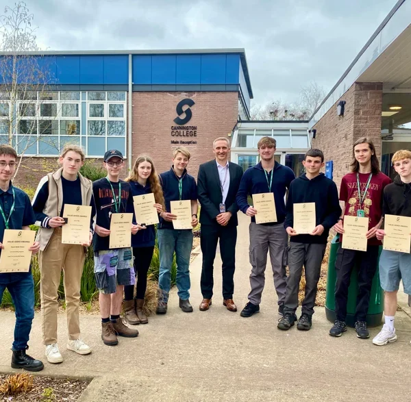 Group of students and teachers holding certificates outside a school building.