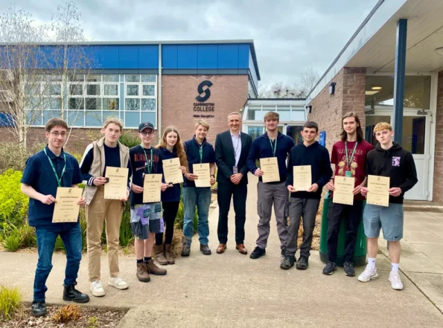 Group of students and teachers holding certificates outside a school building.
