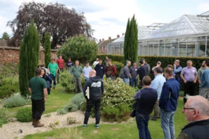 A group of people gathered in a garden with a greenhouse.