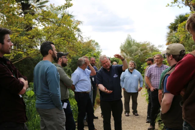 A group of men standing outside in a garden or orchard.