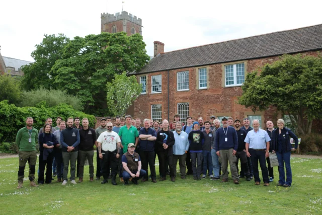 A group of people posing for a photo on grass in front of a large brick building.