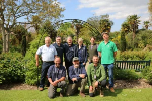 A group of nine people posing for a photo in a garden on a sunny day.