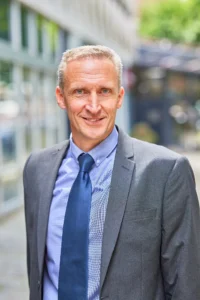 A middle-aged man in a suit standing on a city sidewalk.