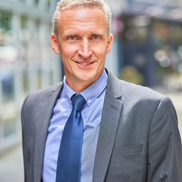 A middle-aged man in a suit standing on a city sidewalk.