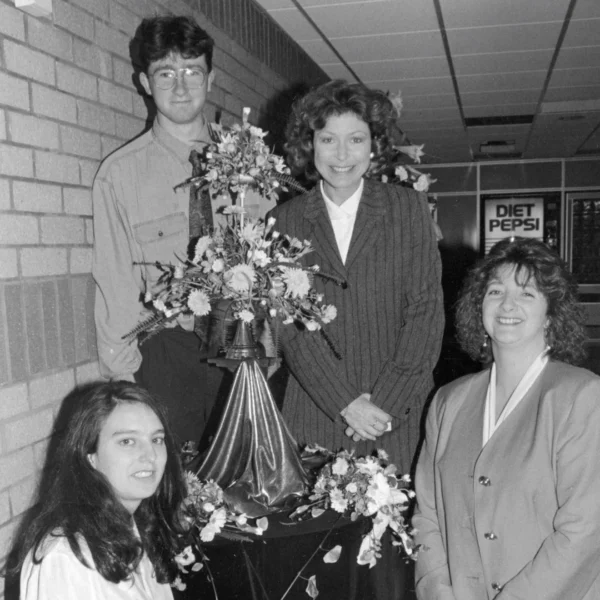 Four people posing with floral arrangements, smiling for the photo.