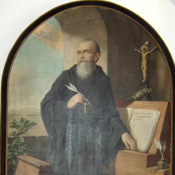 A man with a long grey beard wearing a dark robe standing next to a lectern with a book on it.