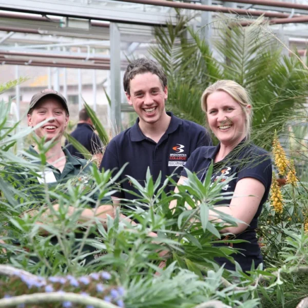 Three people standing among plants in a greenhouse setting.