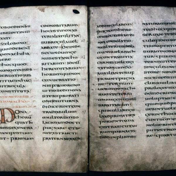 An old, open book with yellowed pages and black text, featuring a large decorative letter.
