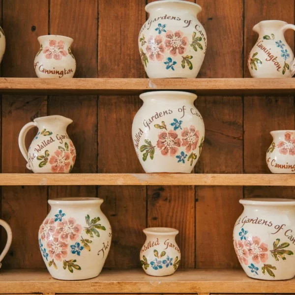 A wooden shelf with various floral ceramic jugs and pitchers