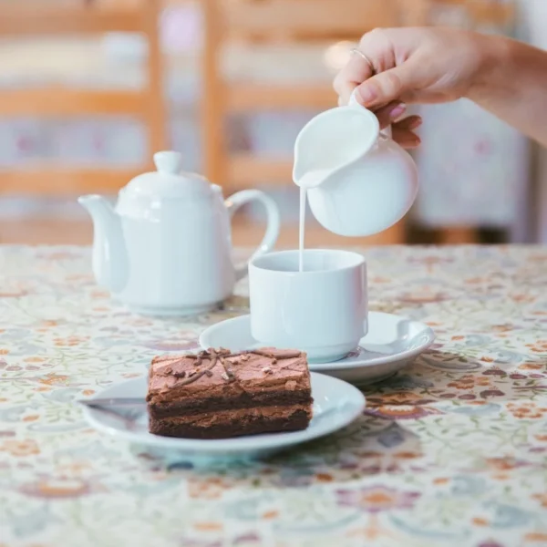 A hand pouring a cup of tea next to a brownie on a plate