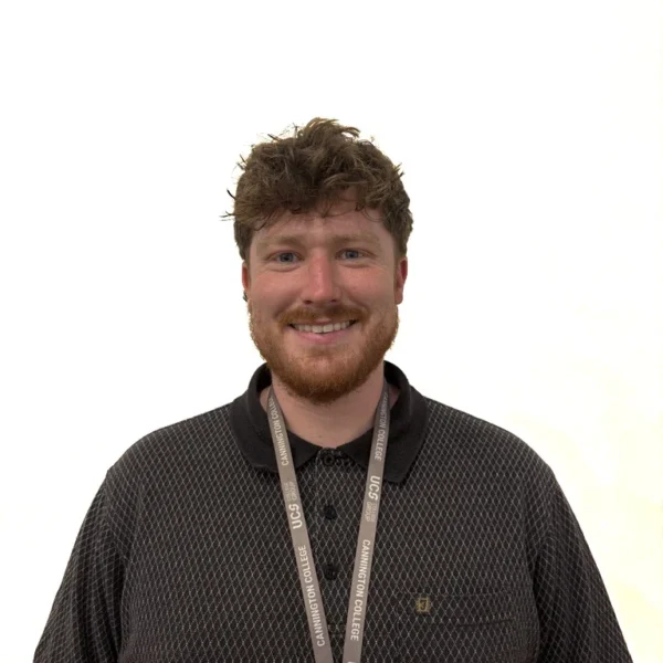 A smiling man with curly hair and a beard wearing a dark polo shirt with a lanyard around his neck.