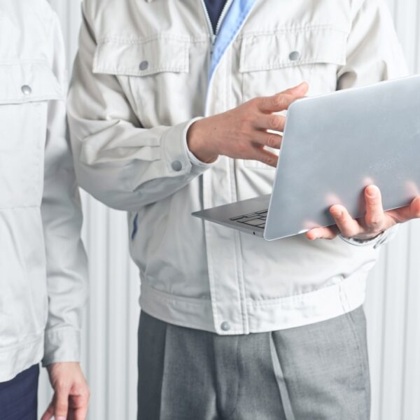 Two engineers in white uniforms are collaborating, one holding a laptop and the other a hard hat.