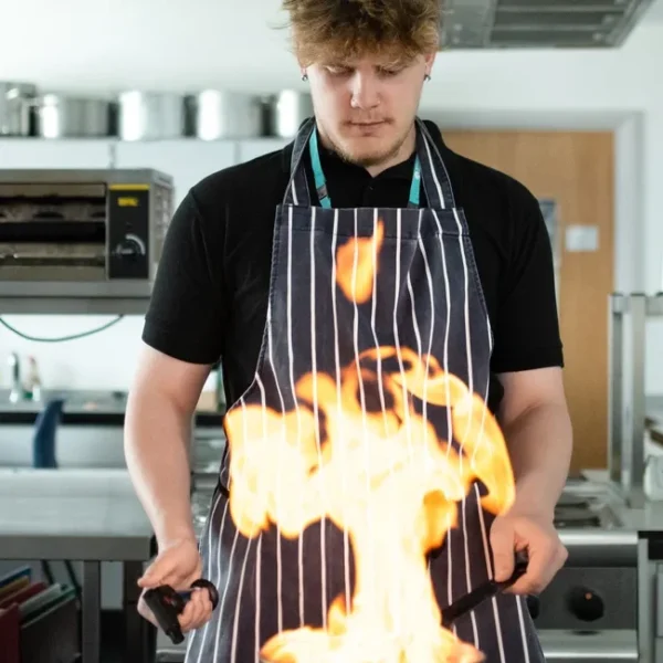 Chef preparing a dish with flaming ingredients in a professional kitchen.