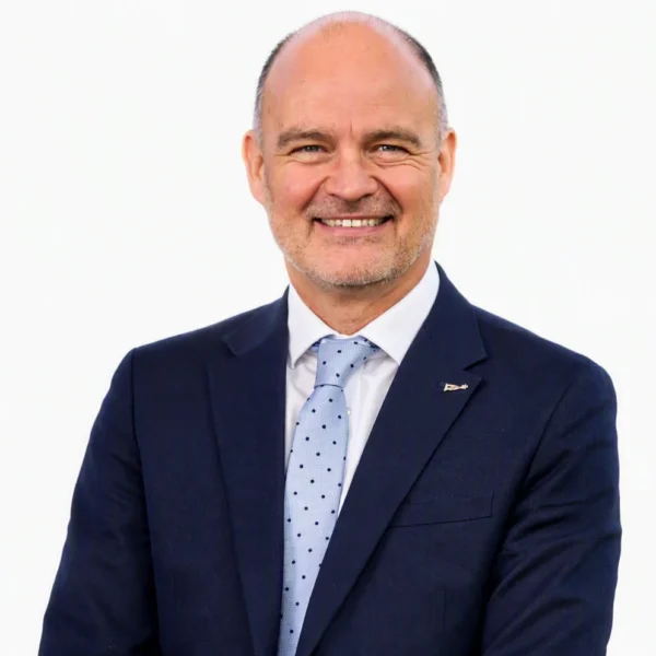 Smiling bald man in a navy suit with light blue polka dot tie.