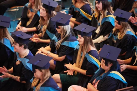 Graduates wearing black gowns and blue caps with yellow trim clapping