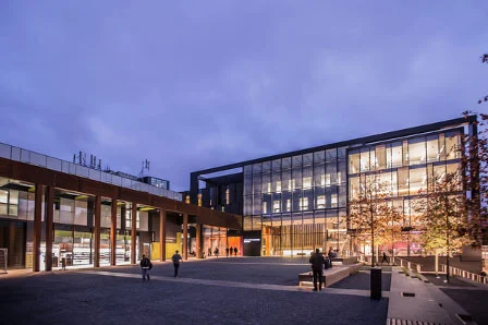 A modern building with glass walls and a large plaza at dusk.