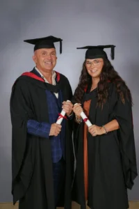 Graduation photo of a man and woman in academic regalia holding rolled up certificates.