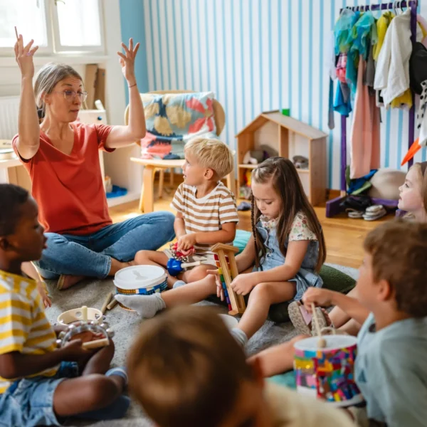 Two teachers and a group of children sitting on the floor in a classroom.