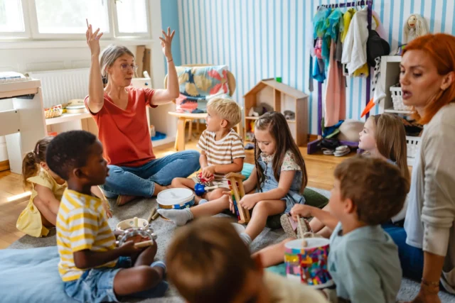 Two teachers and a group of children sitting on the floor in a classroom.