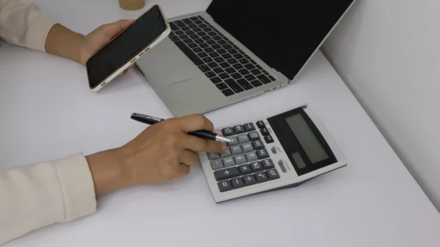 Person using a calculator and holding a tablet.