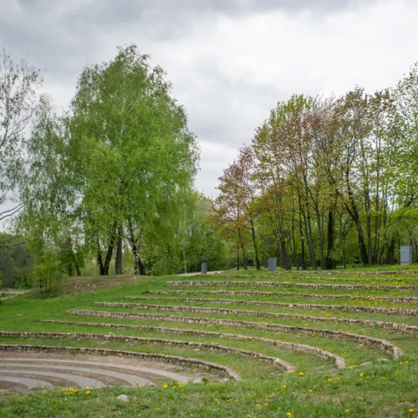 An outdoor amphitheater with curved seating areas surrounded by grass and trees.