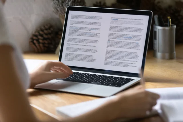 A person sitting at a desk using a laptop with a document on the screen.