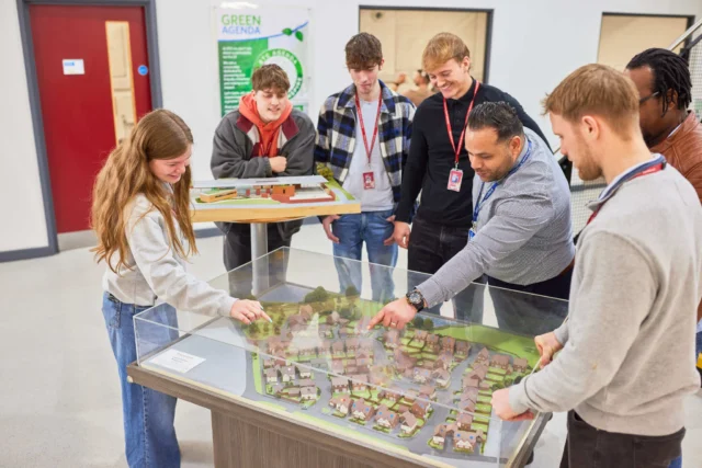Group of students gathered around an interactive table model, exploring urban planning.