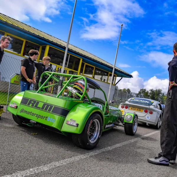 UCS Motorsport's Caterham 7 race car, Esme, is parked on a track with students from the race team standing around it.