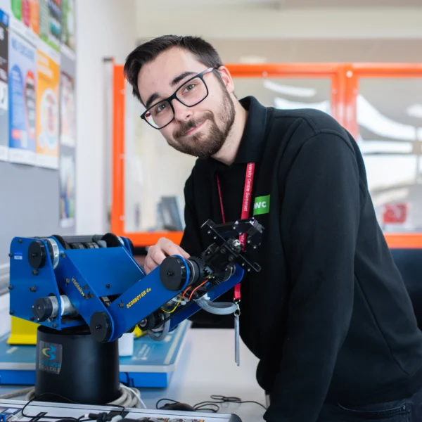 Man working with a blue robotic arm in an industrial setting.