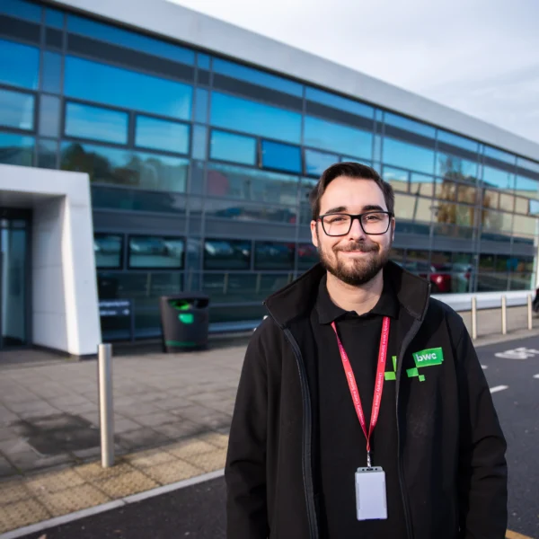 A man stands in front of a modern building with a glass facade.