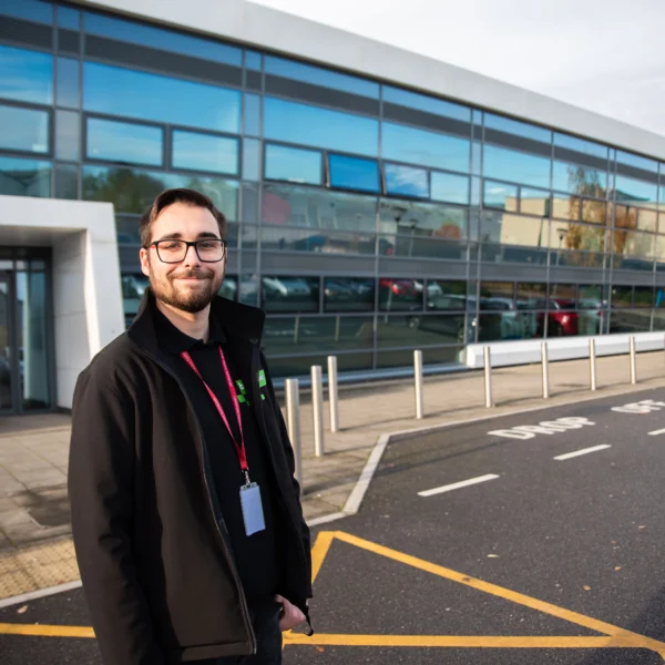 Man in a black coat standing outside a modern building.