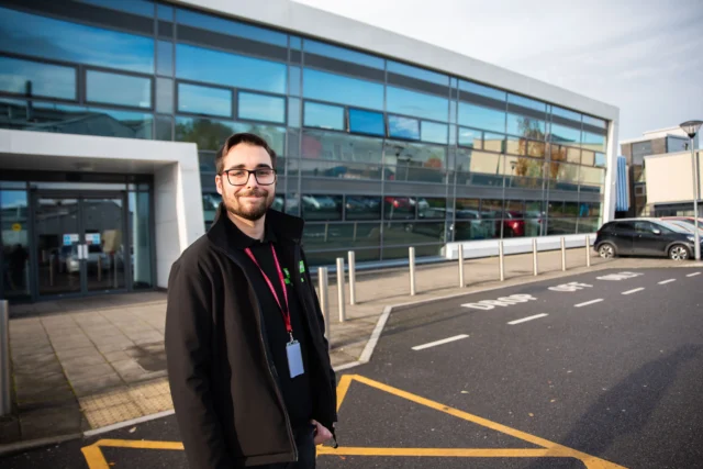 Man in a black coat standing outside a modern building.