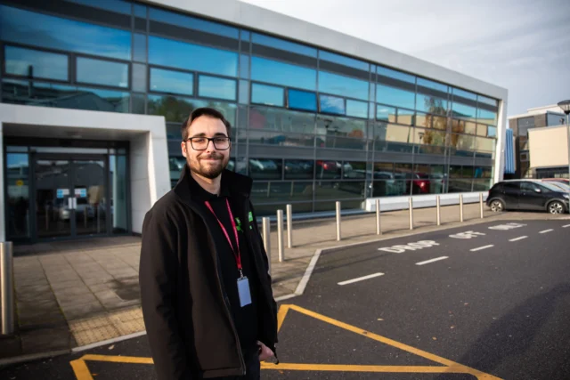 Man standing outside a modern building with a lanyard around his neck.