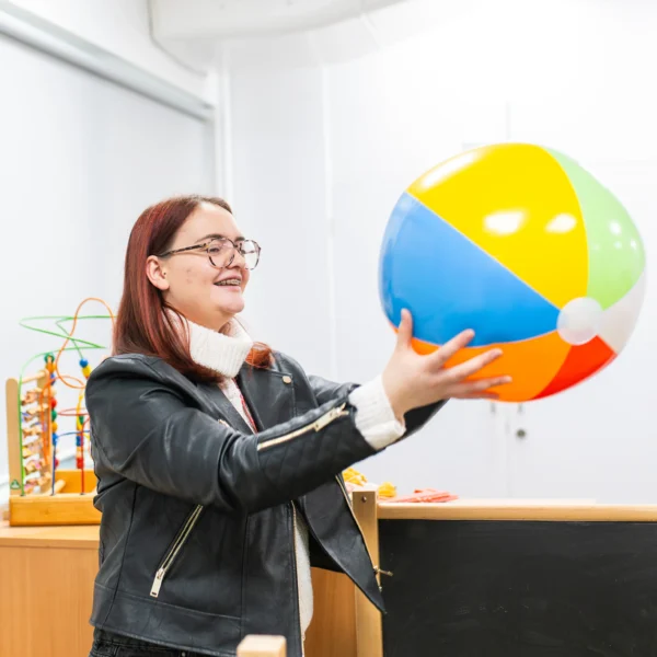 Woman in a black jacket playing with a beach ball in a classroom.