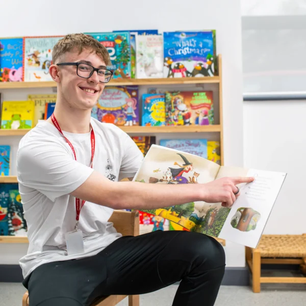 a young man with glasses sitting on a chair reading a book