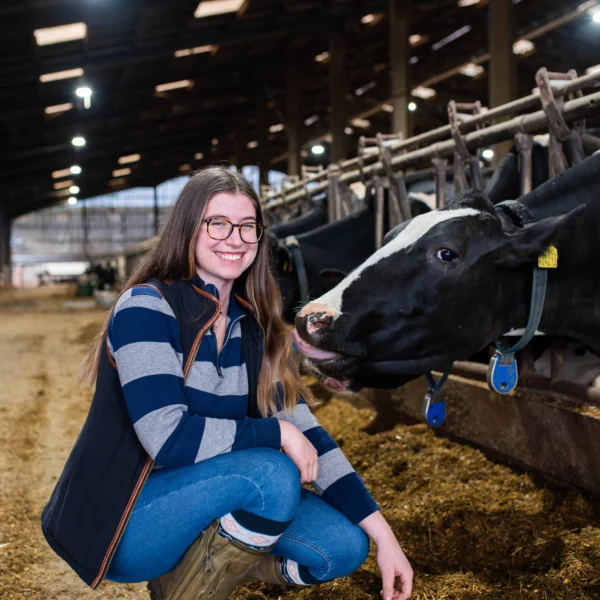 Woman sitting next to cows in a barn, smiling.