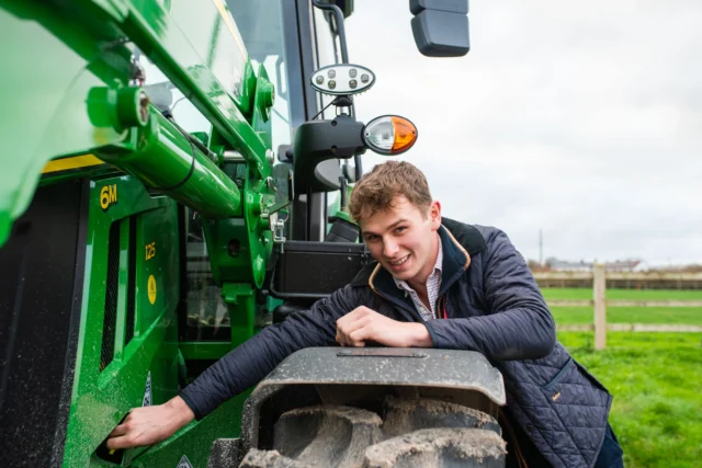 Young man leaning on a green tractor in a field