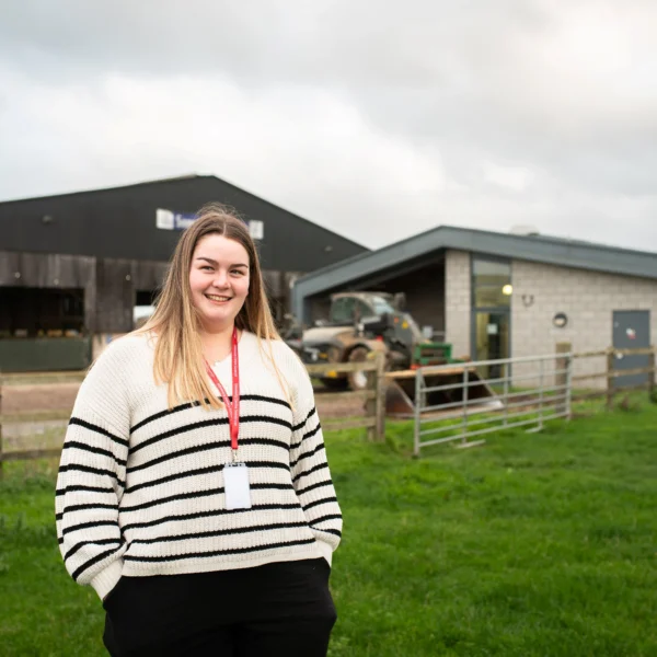 Woman standing in a field with barns behind her.