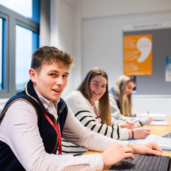 Three students sitting at a desk with laptops in a classroom setting.