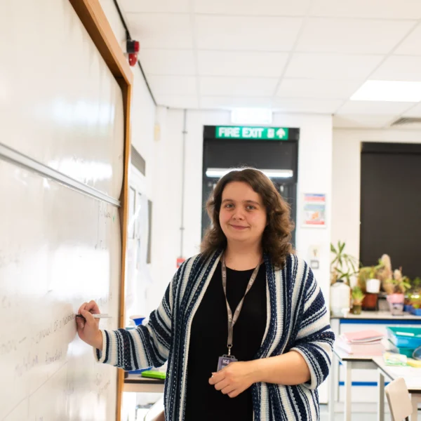 A female teacher writing on a whiteboard in a classroom.