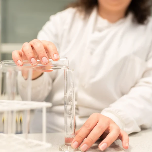A woman in a lab coat and safety glasses handling a test tube.