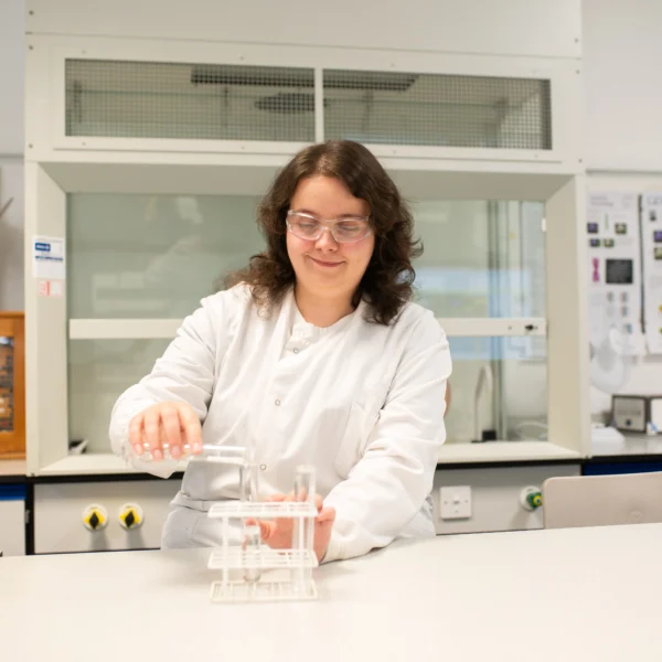Woman in lab coat working in laboratory with beaker and glassware.
