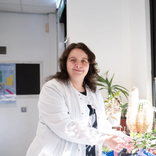Woman in a lab coat standing next to a table with plants and equipment.