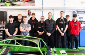 A group of young men standing next to a green race car chassis in a garage.
